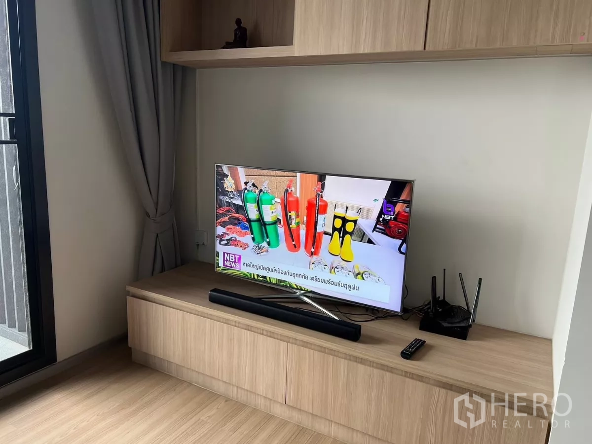 公寓 出租或出售在Chatuchak, Bangkok - 电视放在低矮电视柜上，旁边是落地窗与灰色窗帘。