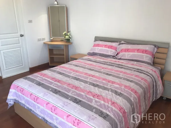 Condominium for rent in Khlong Toei, Bangkok - Primary bedroom with queen bed, wood floors, bedside tables, and a dressing table.