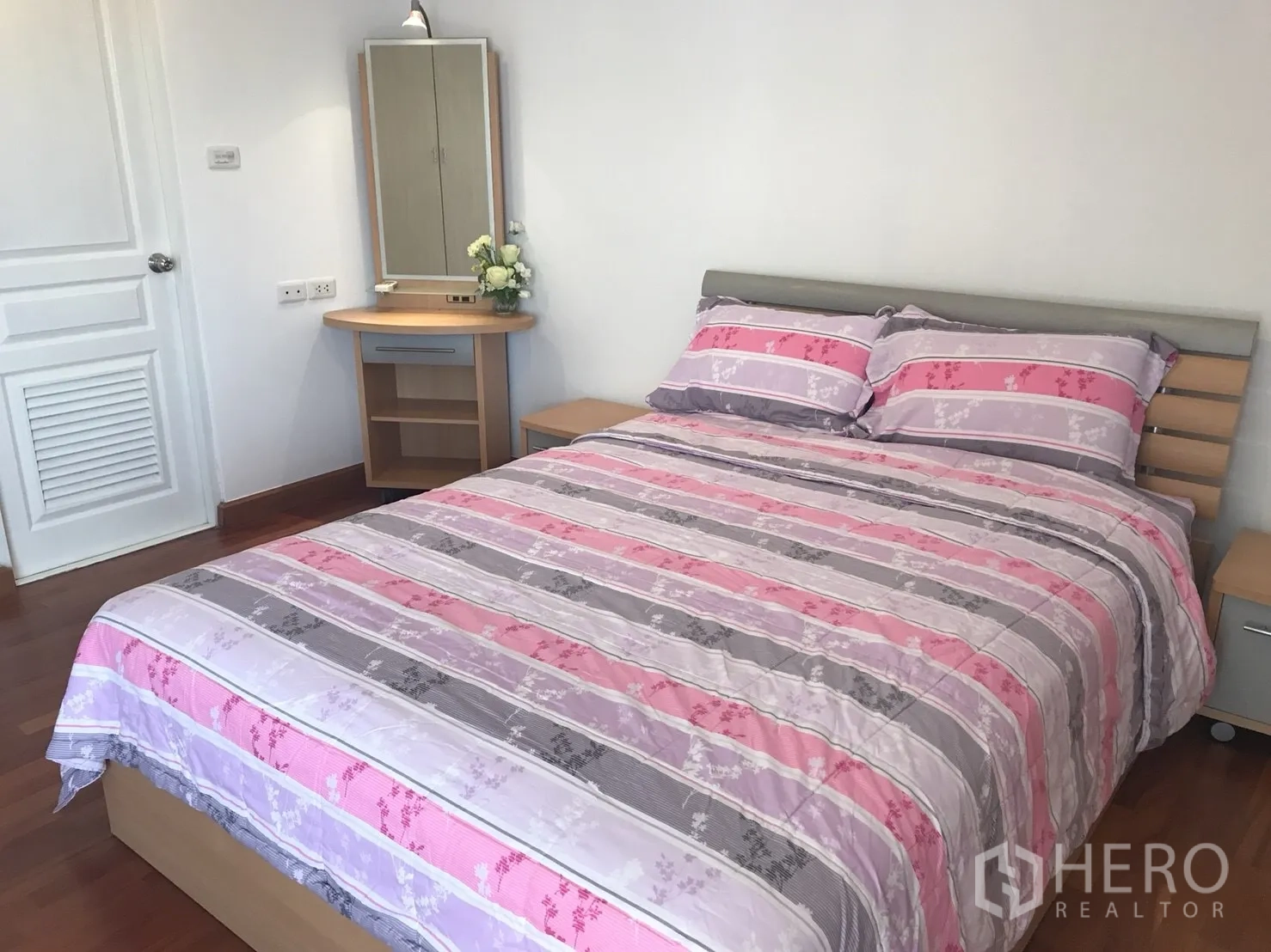 Condominium for rent in Khlong Toei, Bangkok - Primary bedroom with queen bed, wood floors, bedside tables, and a dressing table.