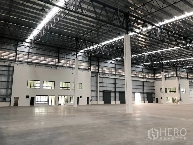 Factory for rent in Samut Prakan - Open production floor with skylit steel beams, smooth concrete slab and several loading doors.