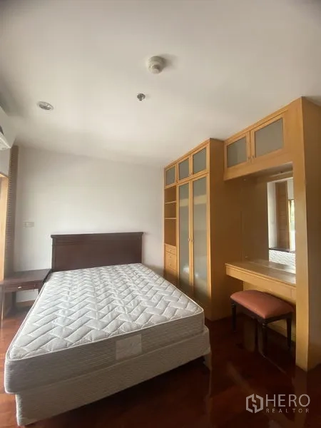 Condominium for rent - Second bedroom with mattress, built-in wardrobes and dressing desk on warm wood flooring.