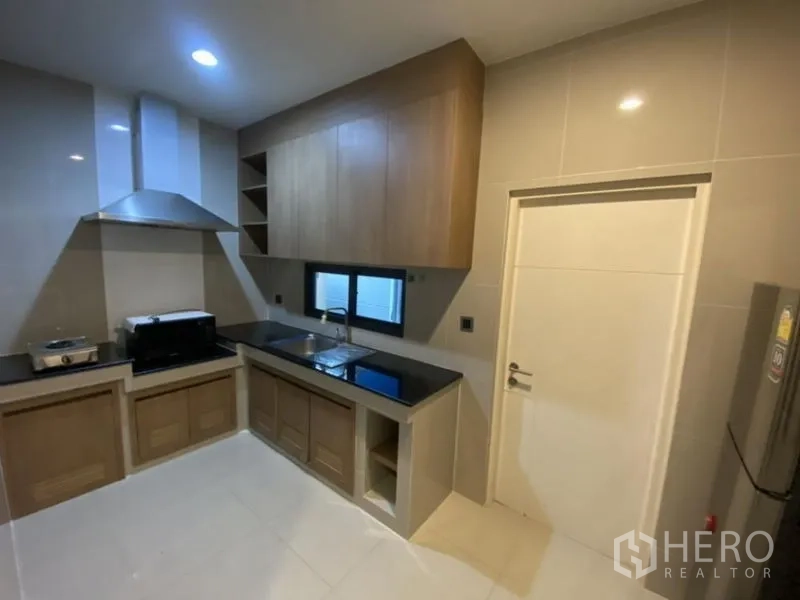 Detached House for rent in Bang Kapi, Bangkok - Fitted kitchen with range hood, upper cabinets, black countertops and sink.