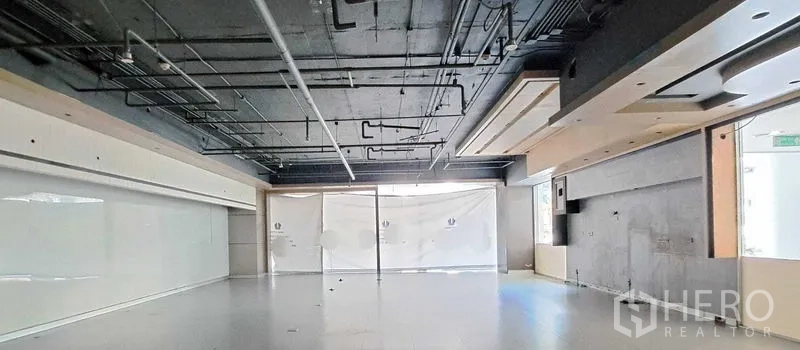 零售空间 出租 - 开放式零售室内，黑色外露天花与管线、浅色地面、整面落地玻璃门面，待二次装修。