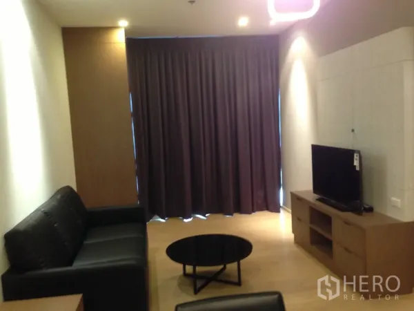 คอนโด ให้เช่าในBangkok - โซนนั่งเล่นพร้อมชั้นวางทีวี โซฟาสีดำ โต๊ะกาแฟ และผ้าม่านยาวเต็มความสูงเพื่อความเป็นส่วนตัว