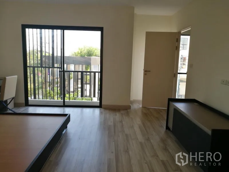 Townhouse for rent in Saphan Sung, Bangkok - Bedroom with wood flooring and sliding glass doors to a balcony.