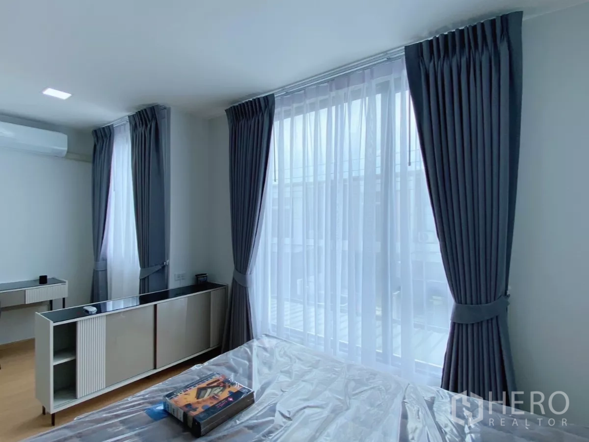 Townhouse for rent in Bang Phli, Samut Prakan - Bedroom wide view with two large curtained windows bringing in daylight.