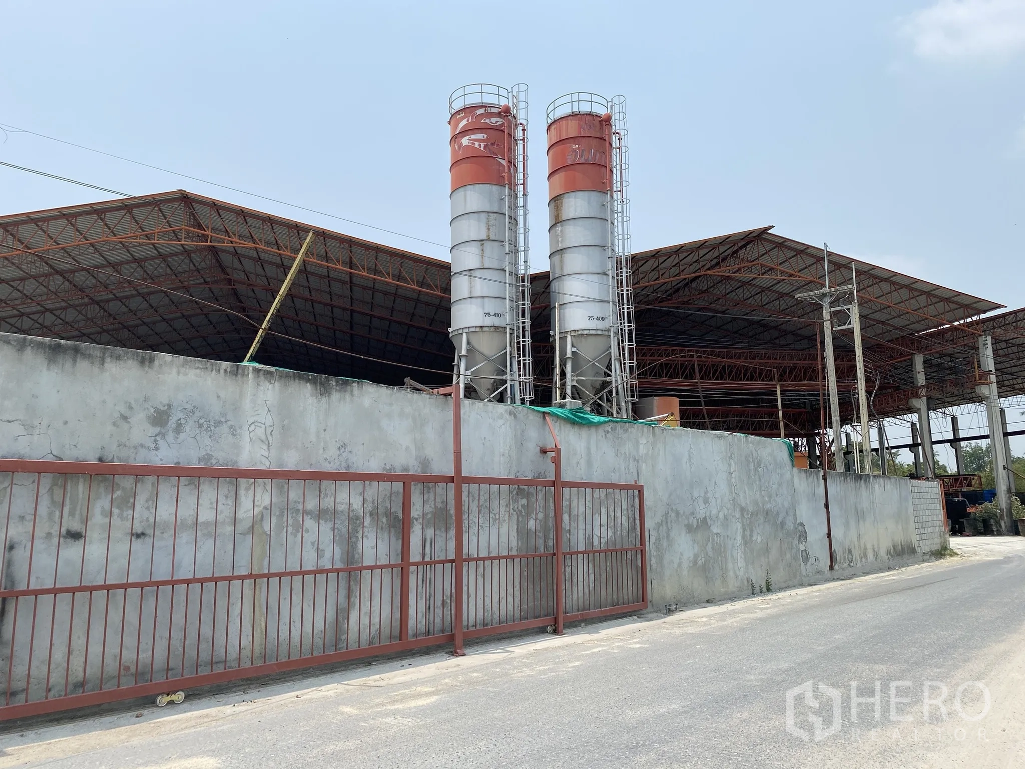 Factory for sale in Mueang Chon Buri, Chon Buri - Exterior wall with twin cement silos beside a large roofed manufacturing shed.
