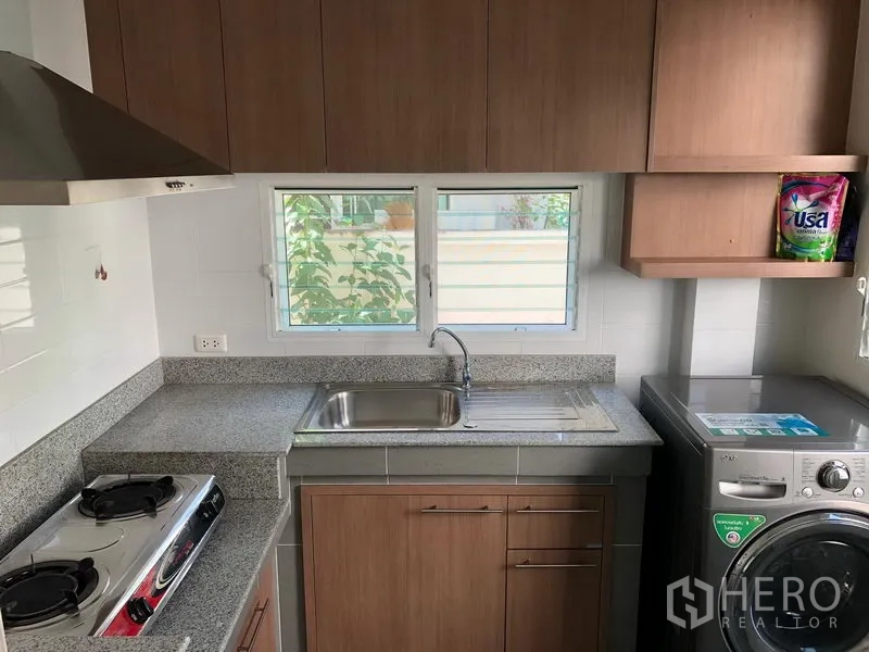 Detached House for rent in Bang Kapi, Bangkok - Fitted kitchen with hob, sink, wood cabinets and a washing machine under the window.