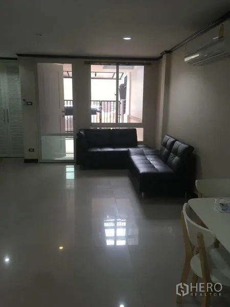 Townhouse for rent in Din Daeng, Bangkok - Bright living area with black L-shaped sofa, glossy floors and sliding doors in a Din Daeng townhouse.