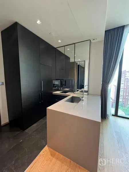 Condominium for rent - Modern kitchenette with stone island, dark built-in cabinets, and floor-to-ceiling window with Bangkok skyline view.
