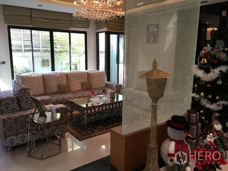 Detached House for rent in Khlong Toei, Bangkok - Bright living room with patterned sofas, crystal chandelier and glass coffee table by large windows.