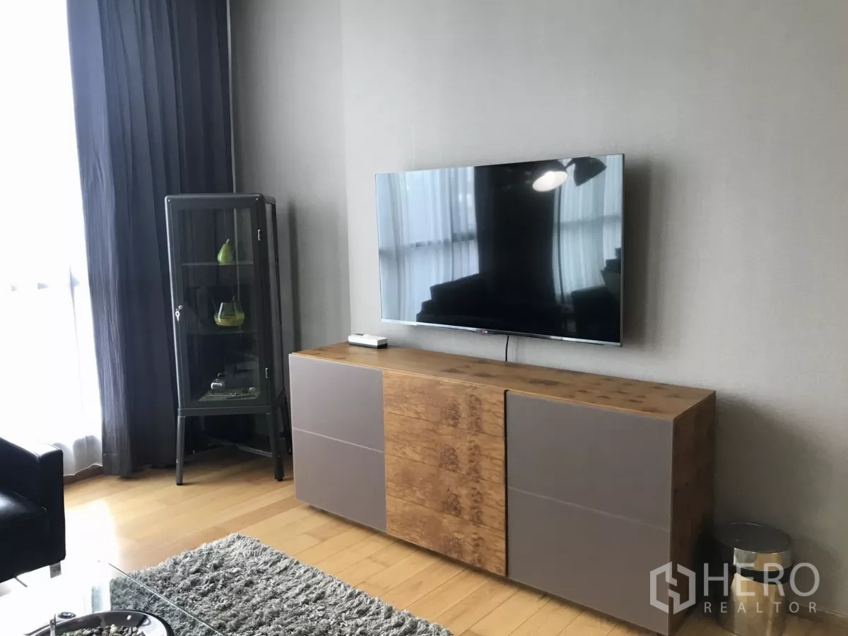Condominium for rent in Watthana, Bangkok - Media wall with wall-mounted TV, wood console and a display cabinet by the window.
