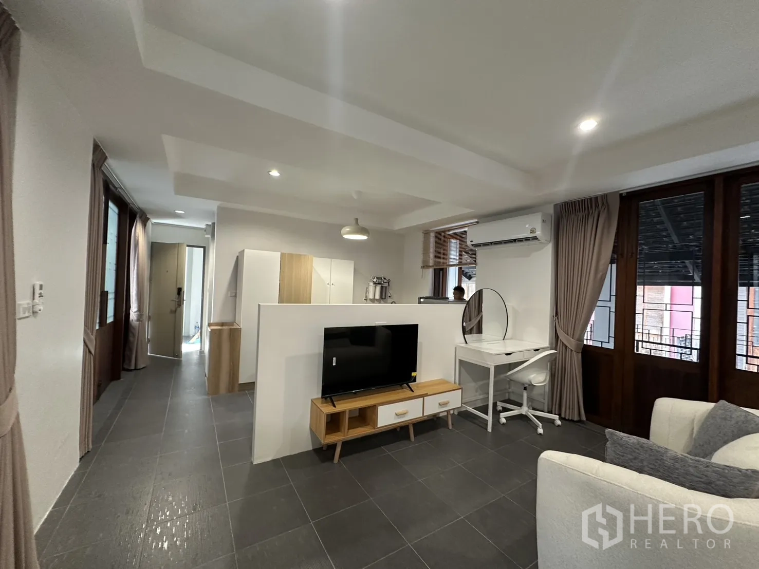 Apartment for rent in Pathum Wan, Bangkok - Open-plan living space with TV console, sofa, desk, and large windows.