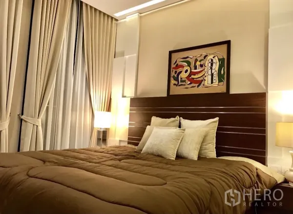 Condominium for rent in Pathum Wan, Bangkok - Cozy bedroom with large bed, warm lighting, artwork and floor-to-ceiling curtains.