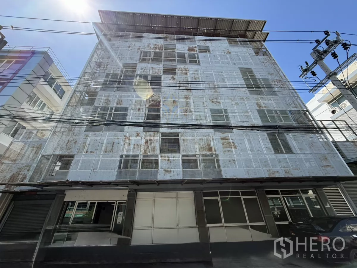Office Space for rent in Bueng Kum, Bangkok - Front exterior of a five-storey office building with perforated metal facade and parking under bright sun.
