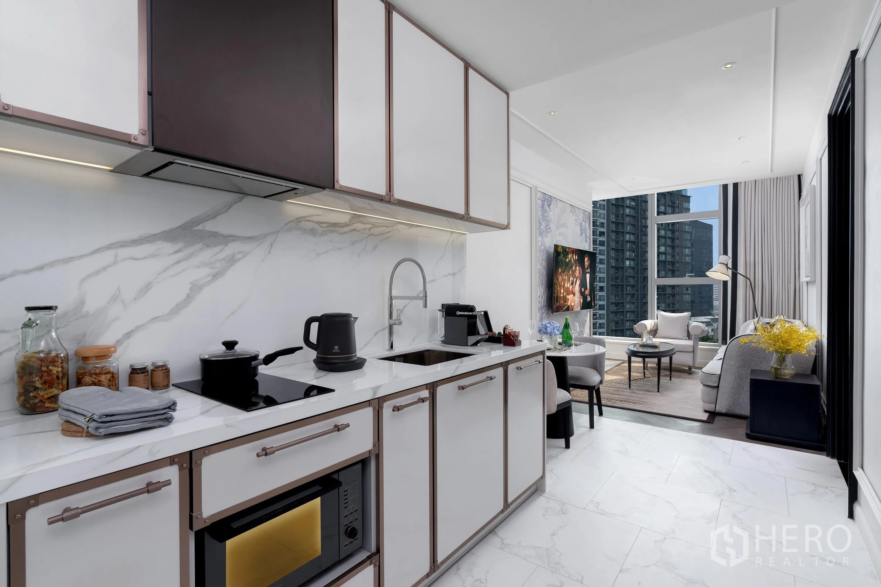 Condominium for rent in Khlong Toei, Bangkok - Sleek kitchenette with marble backsplash, induction cooktop, microwave, and sink opening to the living area with city views.