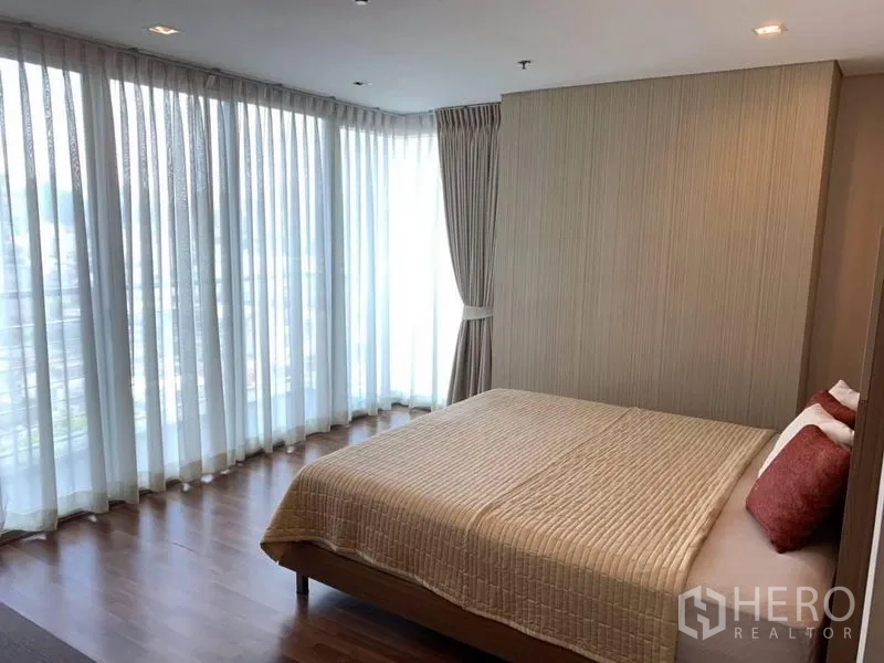 Condominium for rent in Watthana, Bangkok - Corner bedroom with wraparound floor-to-ceiling curtains and city views.