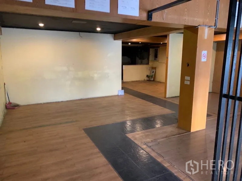 店屋 出租在Watthana, Bangkok - 宽敞的一层开放式空间，木纹地板、嵌灯与结构立柱。