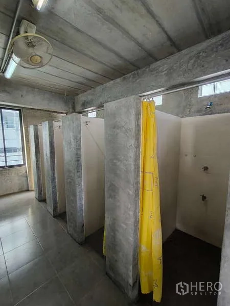 Warehouse for rent in Huai Khwang, Bangkok - Row of individual concrete shower stalls with a yellow curtain inside the facility.