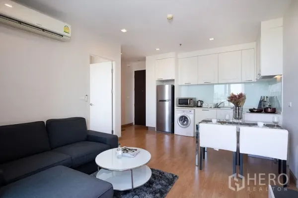 Condominium for rent in Watthana, Bangkok - Open-plan living room and compact kitchen with fridge, washing machine, dining set and sofa near BTS On Nut.