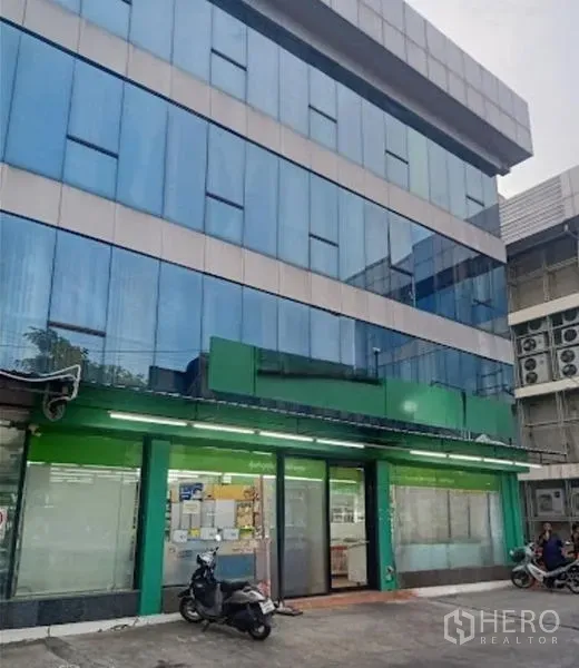 Warehouse for rent in Suan Luang, Bangkok - Four-storey blue-glass commercial warehouse building with ground-floor shopfront and parking area.