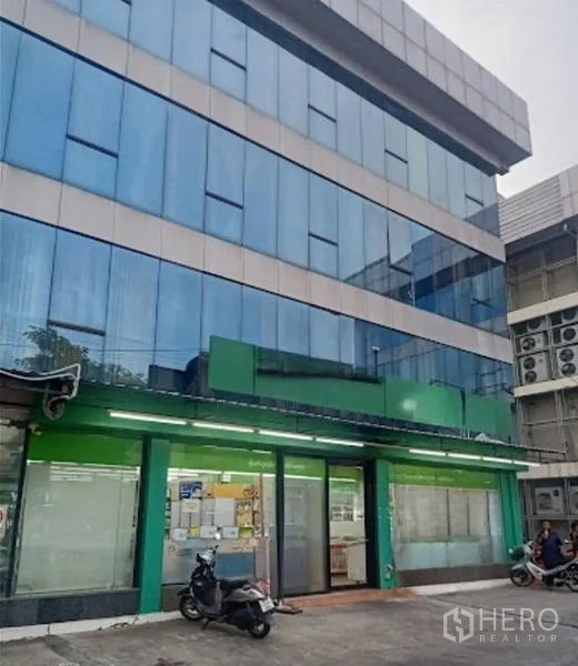 Warehouse for rent in Suan Luang, Bangkok - Four-storey blue-glass commercial warehouse building with ground-floor shopfront and parking area.