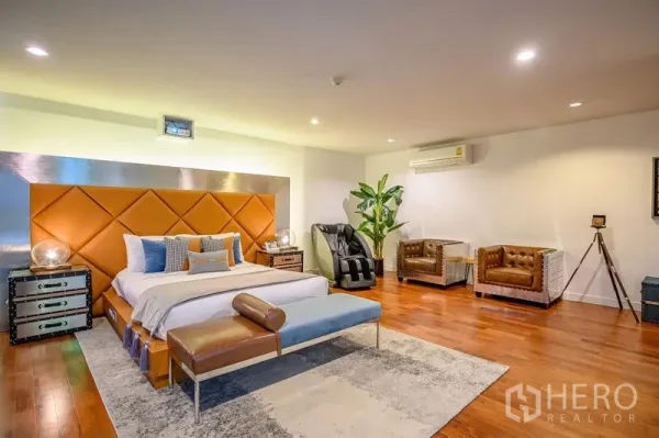 Condominium for rent in Pathum Wan, Bangkok - Spacious master bedroom with orange paneled headboard, wood floors, and a massage chair.