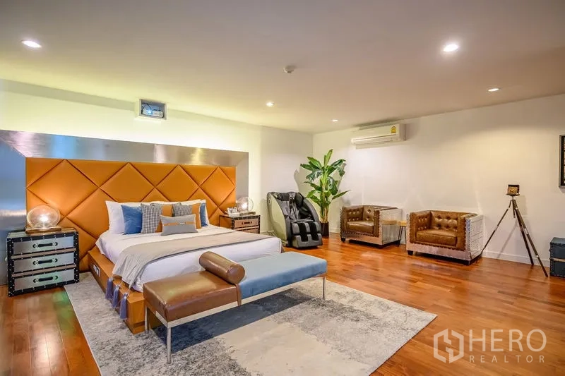 Condominium for rent in Pathum Wan, Bangkok - Spacious master bedroom with orange paneled headboard, wood floors, and a massage chair.