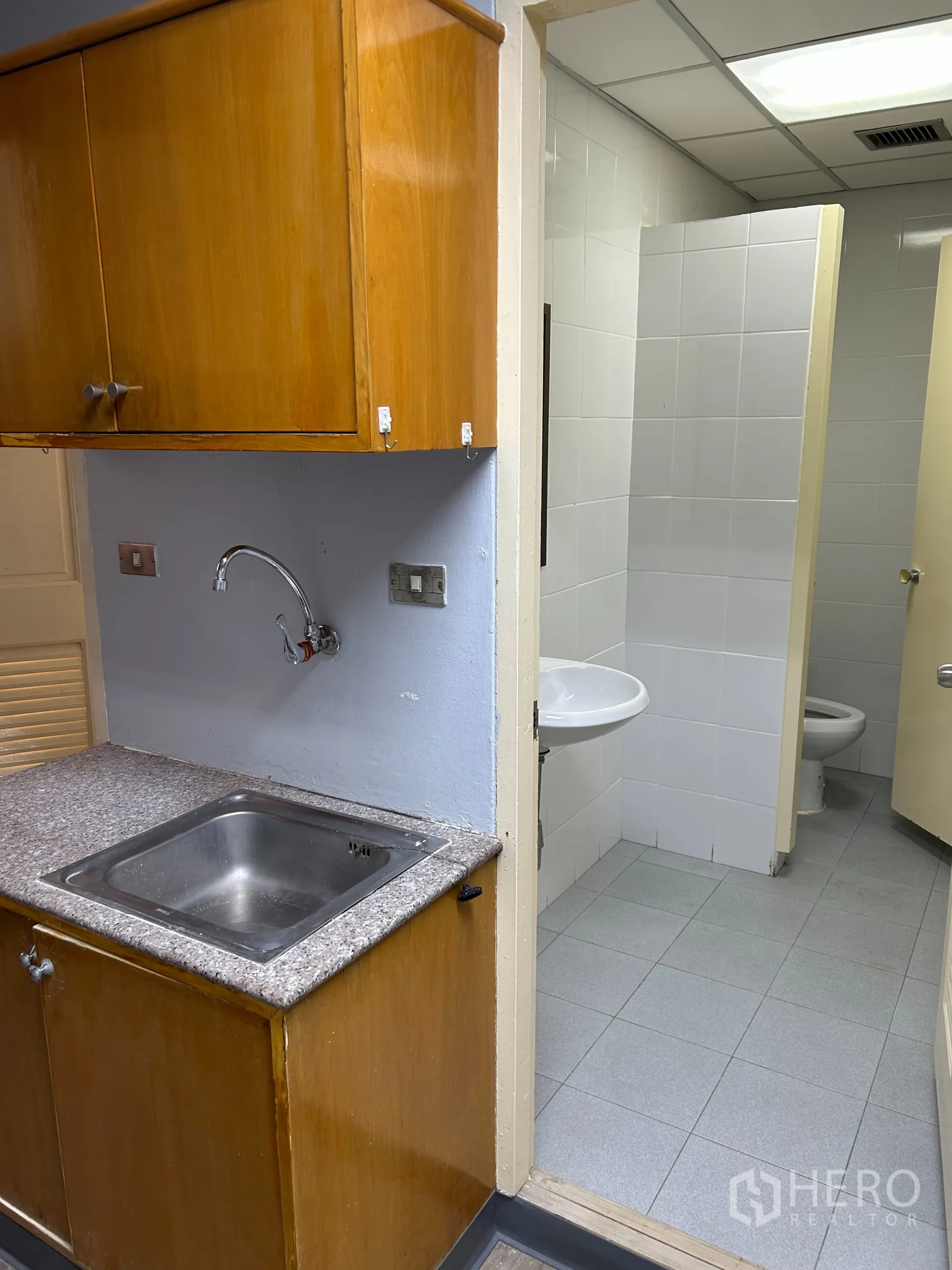 办公空间 出租在Khlong Toei, Bangkok - 茶水间通往套内卫生间，白色瓷砖墙、洗手盆与坐便。