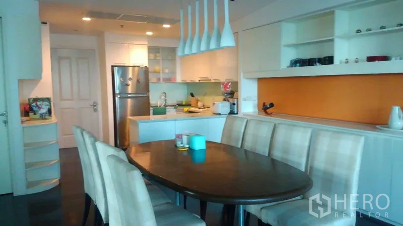 Condominium for sale in Bang Rak, Bangkok - Open-plan dining area with six-seat table, pendant lights and a white kitchen with stainless fridge.