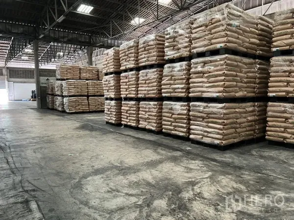 Warehouse for rent in Mueang Samut Prakan, Samut Prakan - Storage zone inside the warehouse with tall stacks of palletized bagged goods under bright lighting and a high ceiling.