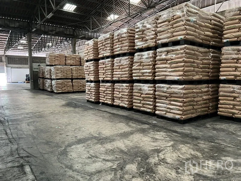 Warehouse for rent in Mueang Samut Prakan, Samut Prakan - Storage zone inside the warehouse with tall stacks of palletized bagged goods under bright lighting and a high ceiling.