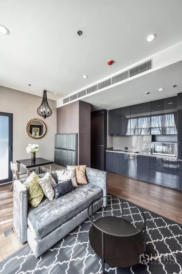 公寓 出租或出售在Bang Rak, Bangkok - 开放式客厅，柔软沙发、餐饮卡座、图案地毯与亮面厨房柜体。