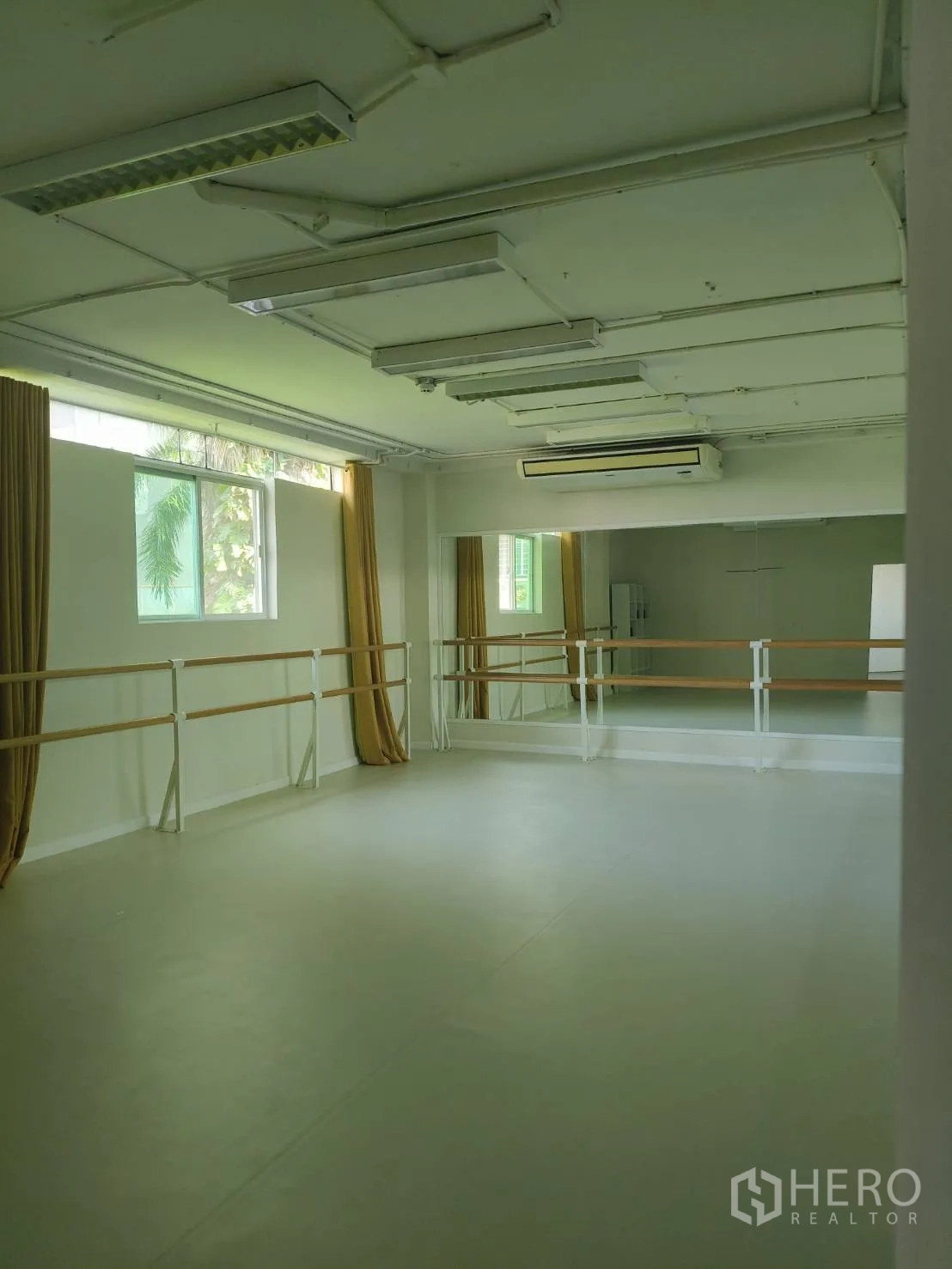 Office Space for rent in Khlong Toei, Bangkok - Spacious studio-style office interior with mirrored wall, ballet barres, windows with curtains, air conditioning and fluorescent lighting.
