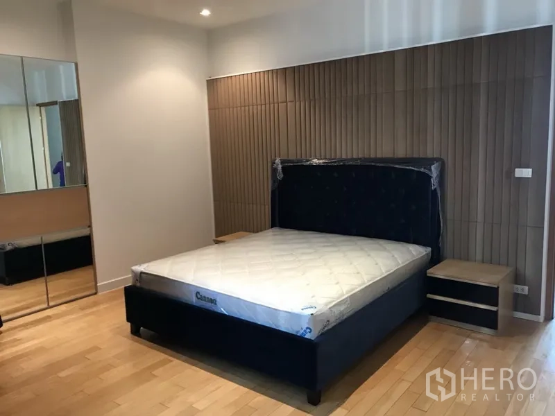 คอนโด ให้เช่าในKhlong Toei, Bangkok - ห้องนอนหลักกว้าง เตียงบุผ้า ผนังลายไม้ และตู้เสื้อผ้าบานกระจก