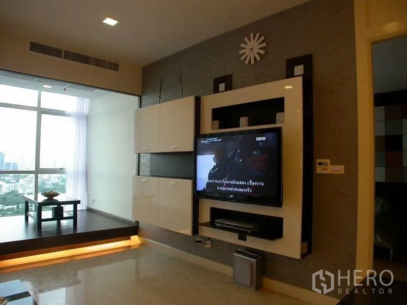Condominium for rent in Khlong Luang, Pathum Thani - Living room with built-in TV wall, large windows and an elevated city-view sitting nook.
