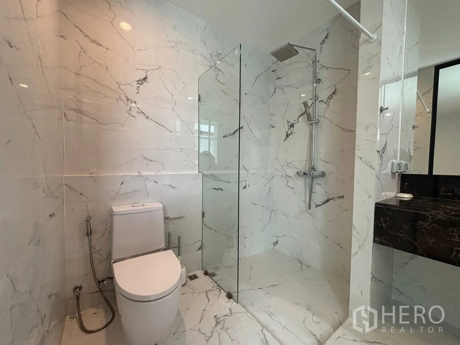 Townhouse for rent in Saphan Sung, Bangkok - Bathroom finished in white marble tiles with a glass-enclosed shower and toilet.