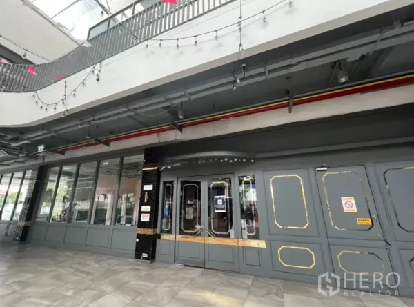 零售空间 出租在Khlong Toei, Bangkok - 商铺入口带镶框门扇，楼上串灯与顶棚设备清晰可见。