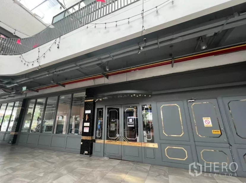 零售空间 出租在Khlong Toei, Bangkok - 商铺入口带镶框门扇，楼上串灯与顶棚设备清晰可见。