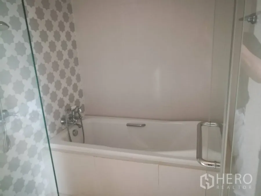 公寓 出售在Khlong Toei, Bangkok - 现代浴室，白色浴缸、灰色图案瓷砖与玻璃隔断。