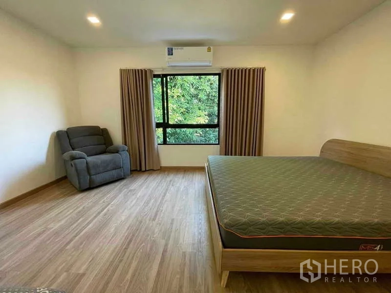 Townhouse for rent or sale in Bang Kapi, Bangkok - Master bedroom with a large window, recliner chair and timber floors.
