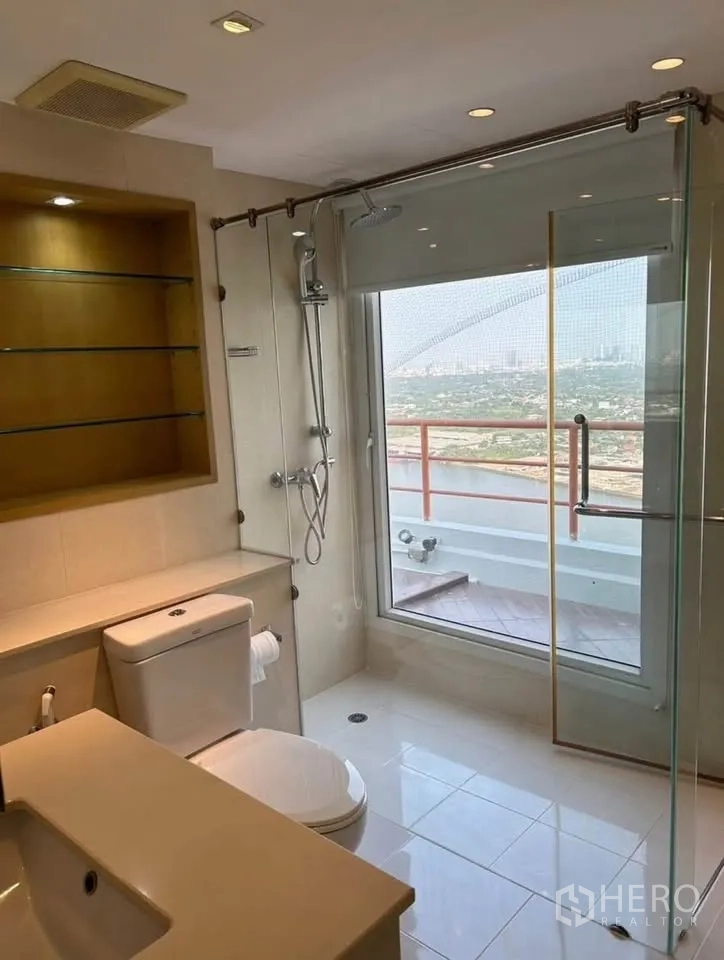 Condominium for rent or sale in Yan Nawa, Bangkok - Modern bathroom with glass shower, large window overlooking the river and built-in shelving.