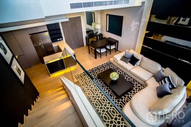 Condominium for rent in Khlong San, Bangkok - Open-plan living area with sectional sofa, dining set and sleek kitchen viewed from the staircase in a modern Bangkok condo.