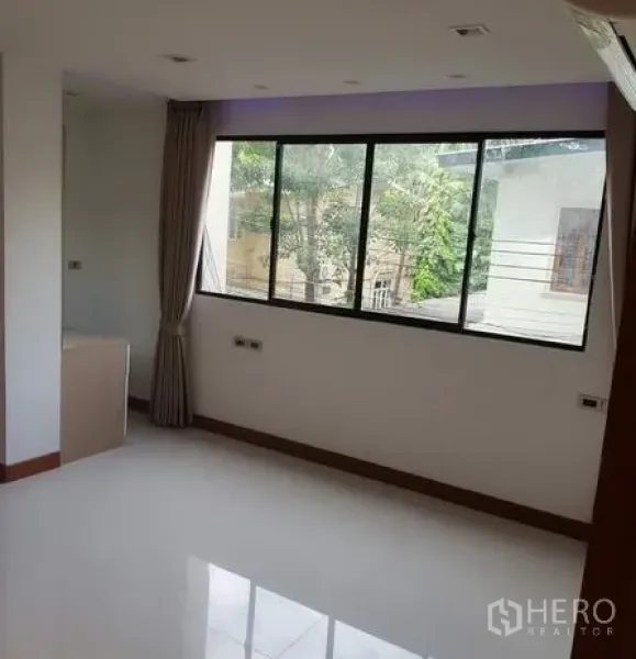 Apartment for rent in Khlong Toei, Bangkok - Sunlit room with wide corner window, glossy white flooring, and green garden outlook.