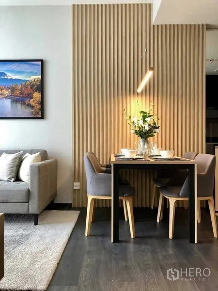 Condominium for rent in Watthana, Bangkok - Dining table beside a cozy sofa and wall art, highlighted by a textured wood panel feature wall.