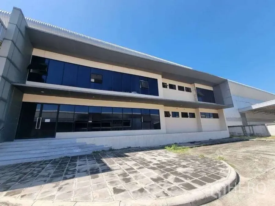 工厂 出租在Bang Pakong, Chachoengsao - 现代化两层厂房外立面，带玻璃办公区与铺装车道，蓝天下视野开阔。