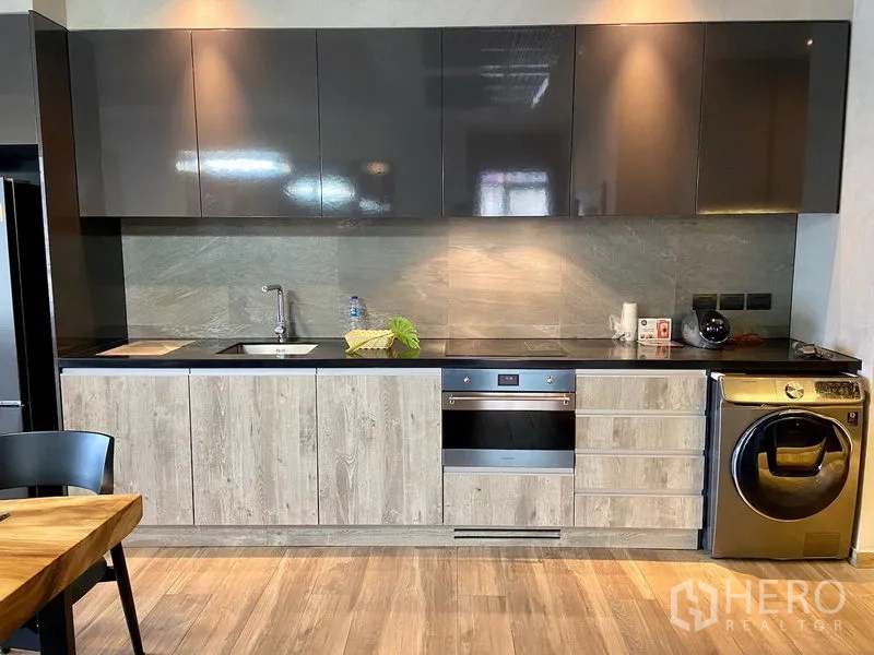 Condominium for rent in Watthana, Bangkok - Full-length modern kitchen with glossy cabinets, built-in oven, sink, and washer-dryer.