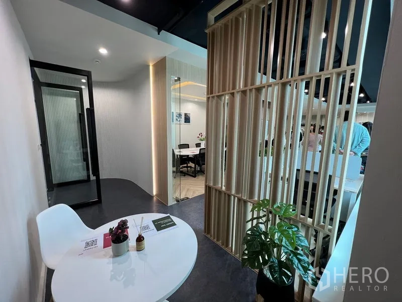 สำนักงาน ให้เช่า - มุมนั่งรอพร้อมโต๊ะกลม ฉากกั้นไม้ และต้นไม้ ข้างห้องประชุม