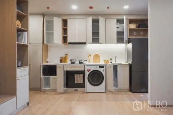 Condominium for sale in Suan Luang, Bangkok - Kitchen shown with cabinet doors open, highlighting ample storage, oven, washer and fridge.