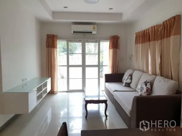 Detached House for rent in Khlong Toei, Bangkok - Bright living room with sofa, TV shelf, air conditioner and glass doors opening to the garden.